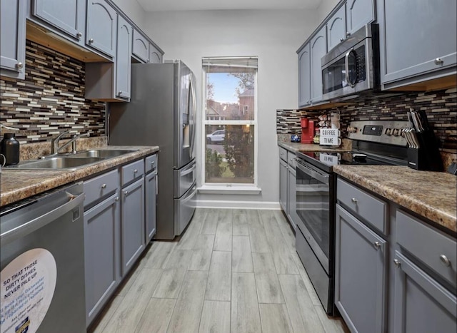 kitchen featuring appliances with stainless steel finishes, light wood-type flooring, a sink, and decorative backsplash