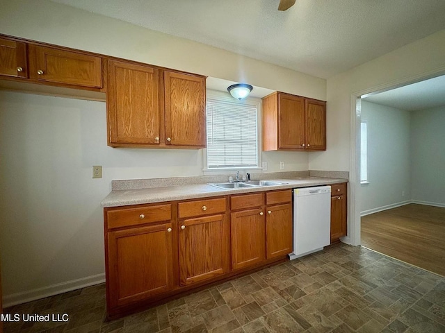 kitchen with light countertops, brown cabinetry, a sink, dishwasher, and baseboards