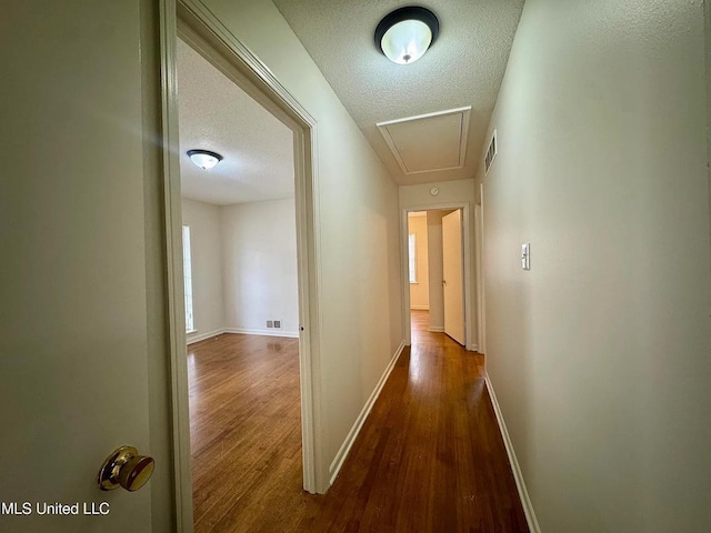 hallway with attic access, baseboards, visible vents, wood finished floors, and a textured ceiling