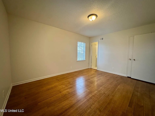 unfurnished bedroom with visible vents, a textured ceiling, baseboards, and wood finished floors