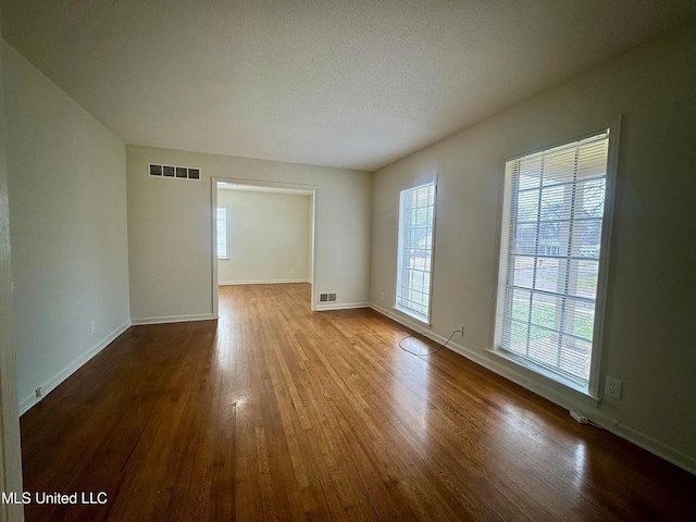 empty room featuring a textured ceiling, wood finished floors, visible vents, and baseboards