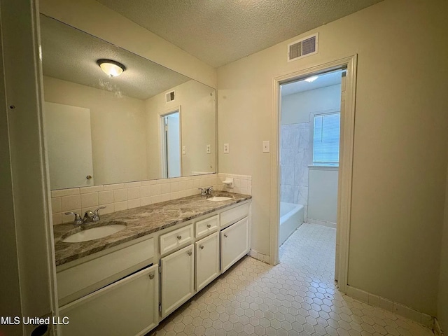 bathroom featuring visible vents, a sink, a textured ceiling, and double vanity