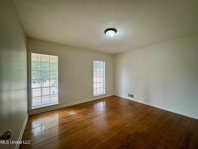 unfurnished room with a textured ceiling, wood finished floors, visible vents, and baseboards