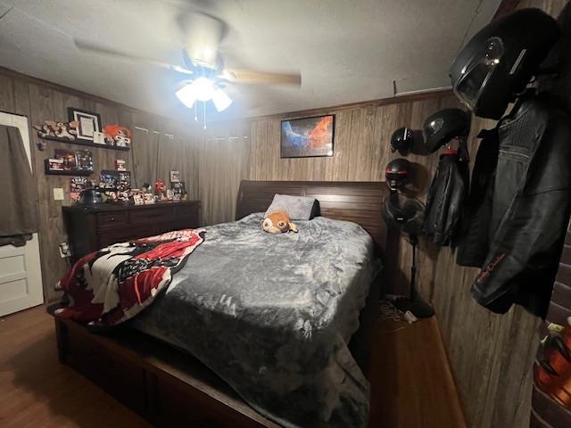 bedroom with ceiling fan, wood walls, and wood finished floors