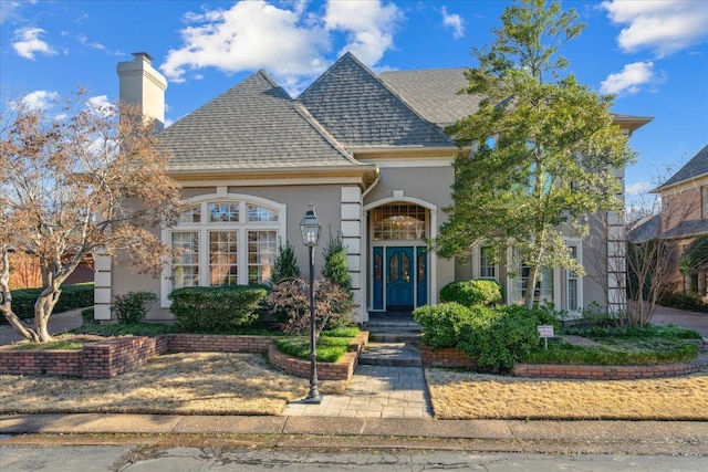 view of front of home featuring a shingled roof, a chimney, and stucco siding