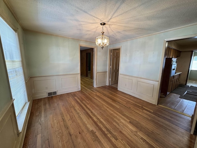 spare room featuring a textured ceiling, a chandelier, wood finished floors, and ornamental molding