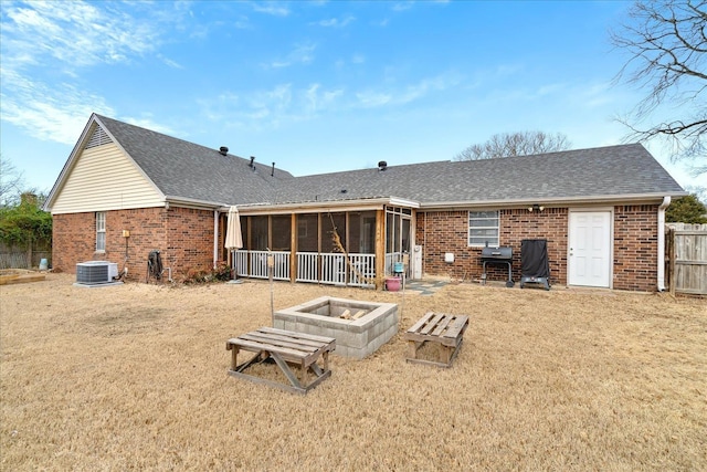 rear view of house featuring a sunroom, an outdoor fire pit, roof with shingles, and brick siding