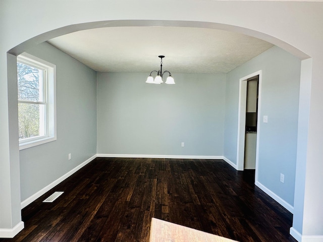 unfurnished room with arched walkways, visible vents, an inviting chandelier, dark wood-type flooring, and baseboards