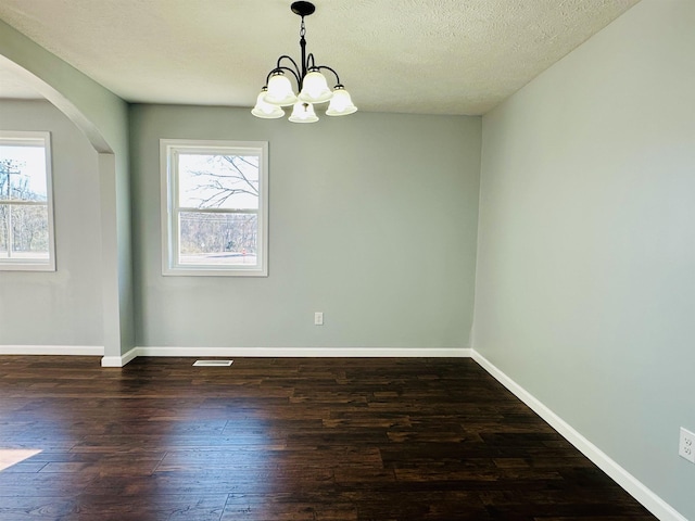 empty room featuring a textured ceiling, dark wood-type flooring, arched walkways, and baseboards