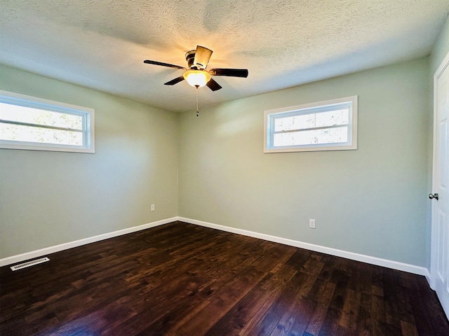 spare room with dark wood-style floors, visible vents, plenty of natural light, and baseboards