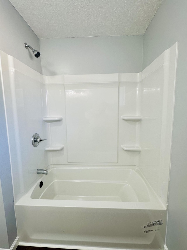 bathroom with a textured ceiling and bathing tub / shower combination