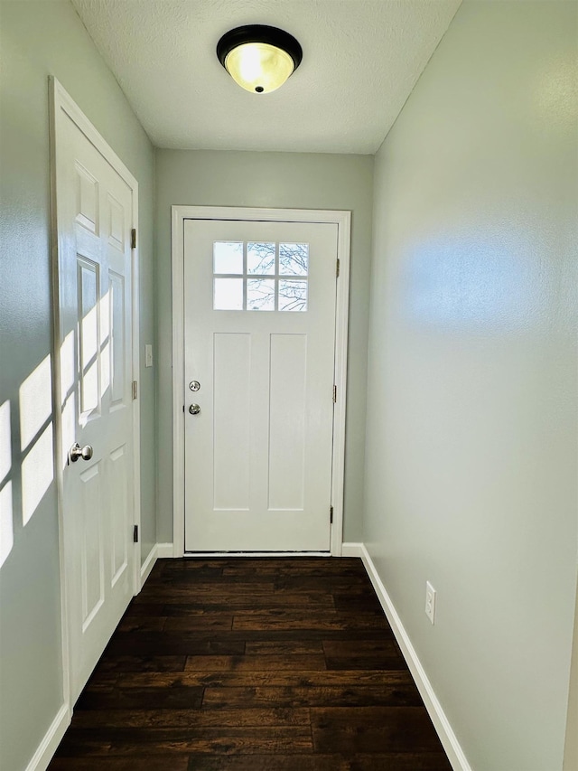 doorway with a textured ceiling, baseboards, and dark wood-type flooring