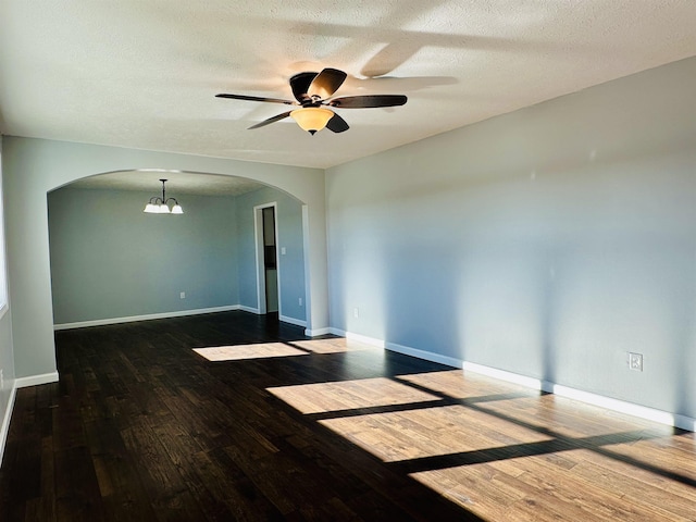 empty room with baseboards, arched walkways, wood finished floors, a textured ceiling, and ceiling fan with notable chandelier