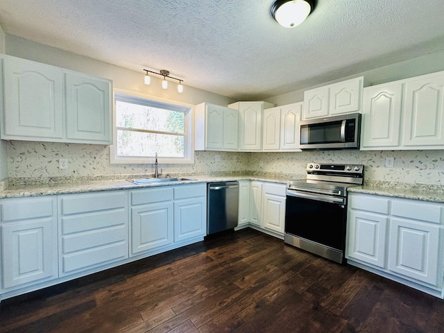 kitchen featuring stainless steel appliances, dark wood-type flooring, a sink, white cabinets, and light stone countertops