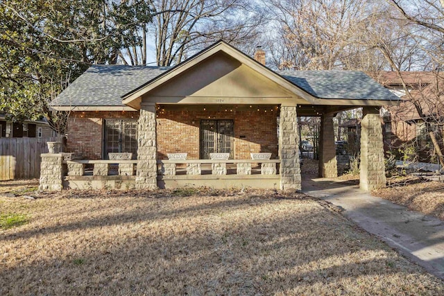 view of front of house with a fenced front yard, brick siding, a chimney, and roof with shingles