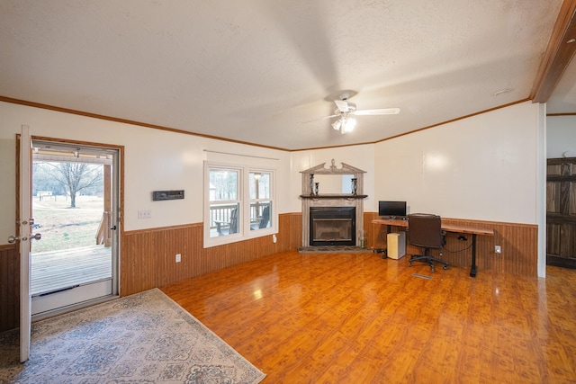 office area featuring a fireplace with raised hearth, wainscoting, wooden walls, a textured ceiling, and wood finished floors