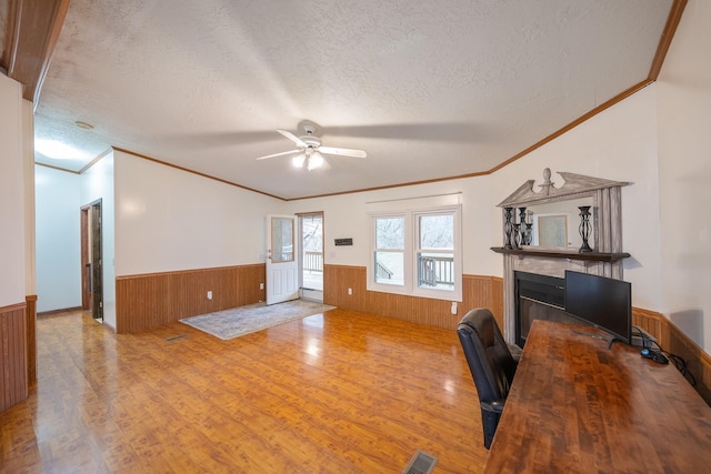 office featuring a wainscoted wall, visible vents, a glass covered fireplace, a textured ceiling, and light wood-type flooring