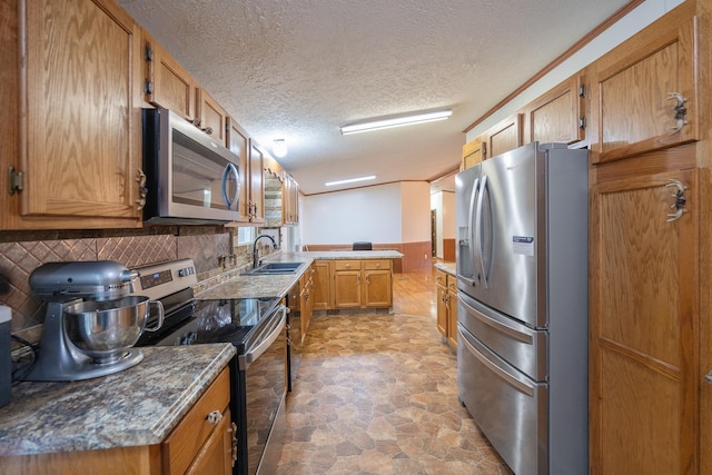 kitchen featuring a wainscoted wall, stainless steel appliances, dark countertops, stone finish floor, and a sink