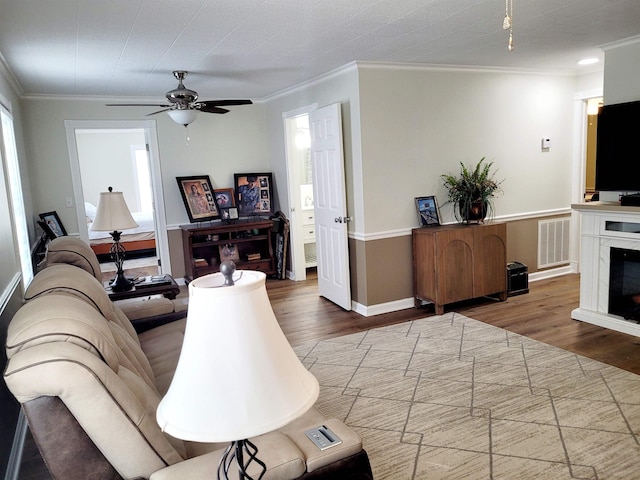 living room with crown molding, a premium fireplace, visible vents, and wood finished floors