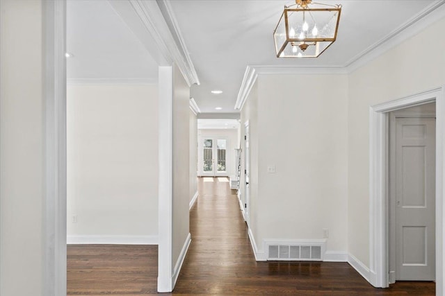 hall featuring dark wood-type flooring, visible vents, baseboards, ornamental molding, and an inviting chandelier