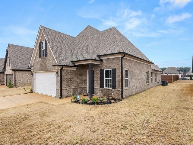 french country style house featuring a shingled roof, central AC, concrete driveway, and brick siding