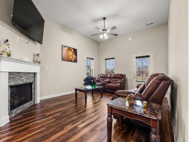 living area featuring dark wood-style floors, a fireplace, visible vents, ceiling fan, and baseboards