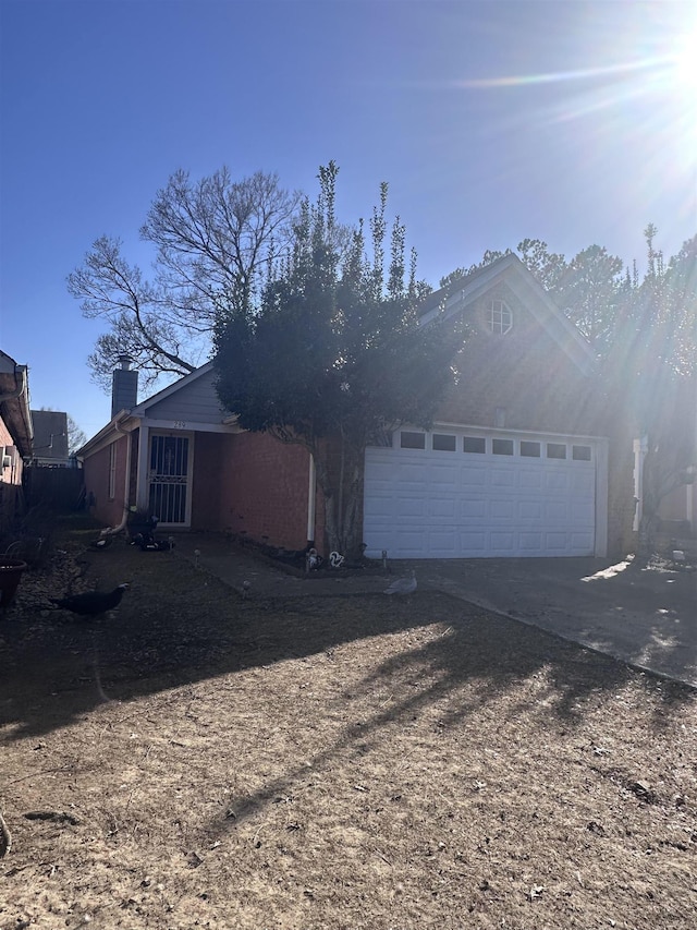 view of side of home with a garage, concrete driveway, and a chimney