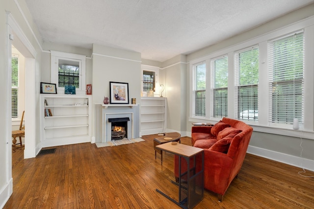 living room featuring dark wood-style floors, a textured ceiling, a fireplace with flush hearth, and visible vents