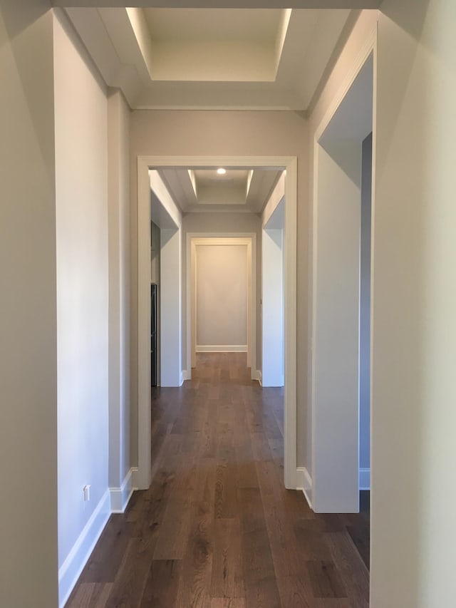 hallway featuring dark wood-type flooring, a tray ceiling, and baseboards