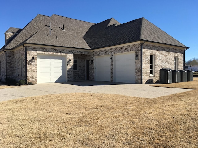 view of side of home featuring cooling unit, a garage, brick siding, concrete driveway, and roof with shingles