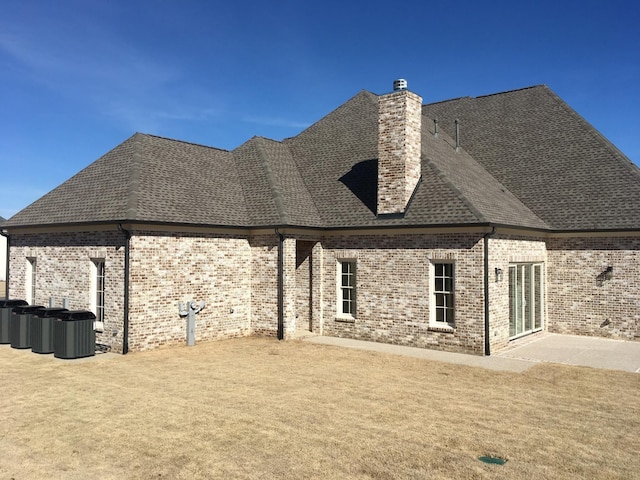 rear view of property with a shingled roof, a chimney, a patio, and brick siding