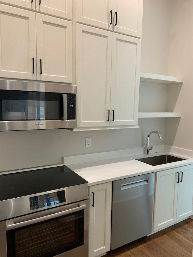 kitchen with wood finished floors, a sink, white cabinets, appliances with stainless steel finishes, and open shelves