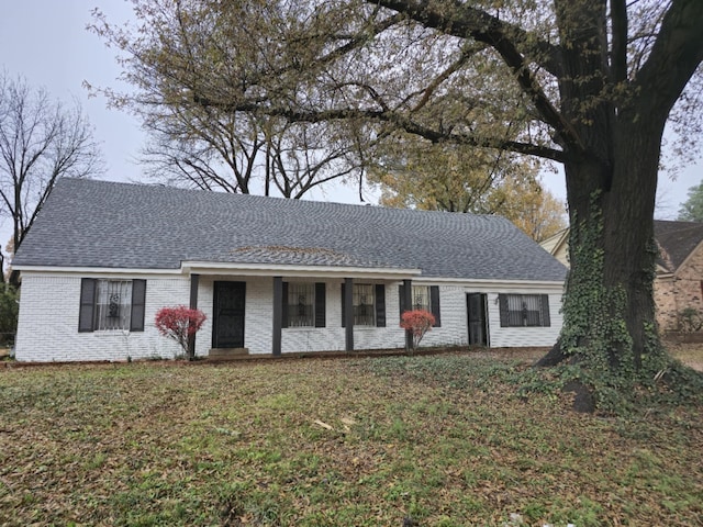 ranch-style home with a shingled roof, a front yard, covered porch, and brick siding