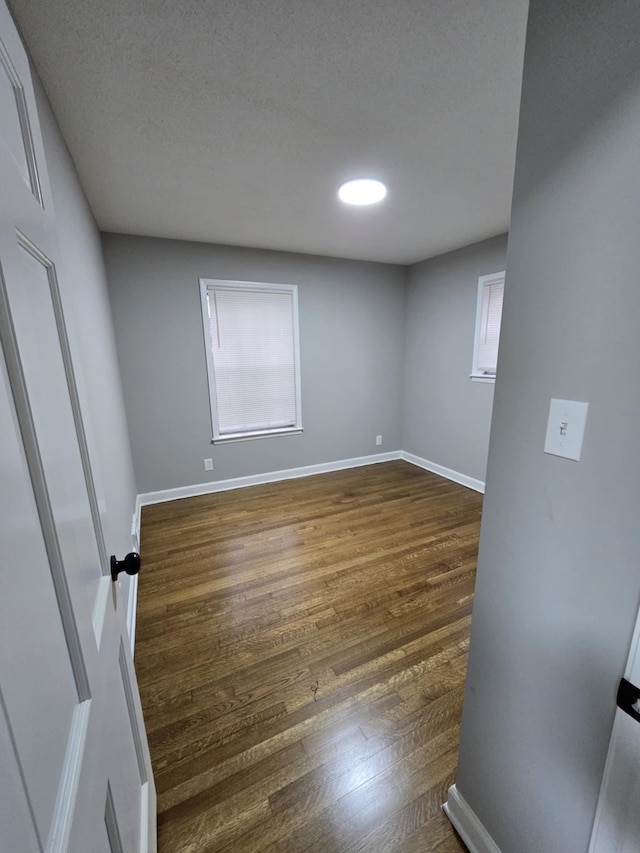 empty room featuring a textured ceiling, baseboards, and dark wood-type flooring