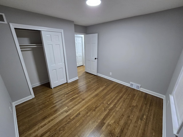 unfurnished bedroom with dark wood-style floors, baseboards, visible vents, and a closet