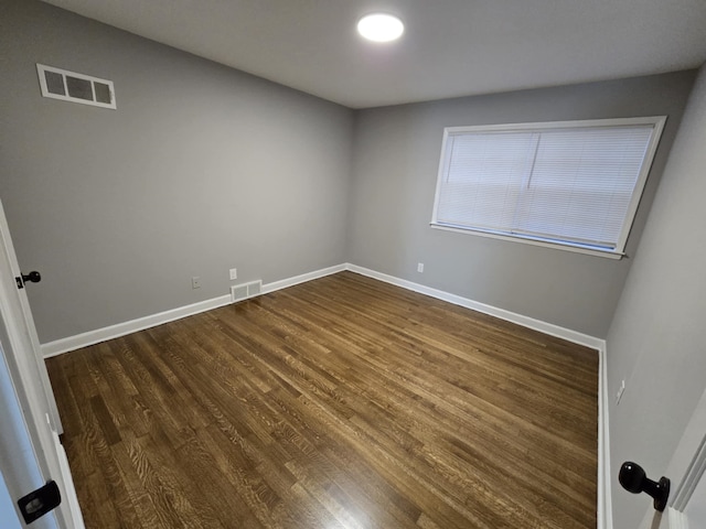 unfurnished room featuring dark wood-type flooring, visible vents, and baseboards