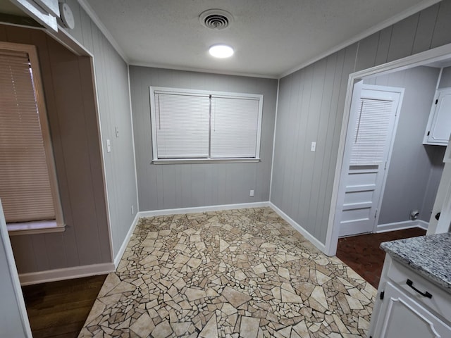 interior space with baseboards, a textured ceiling, visible vents, and crown molding