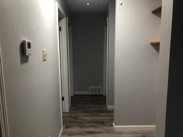 hallway featuring dark wood-style floors, baseboards, and visible vents