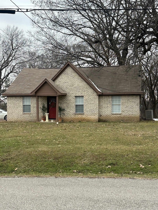 view of front facade featuring a front lawn, a shingled roof, cooling unit, and brick siding