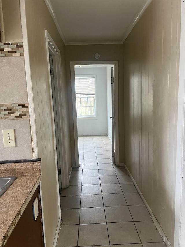 corridor featuring light tile patterned floors, ornamental molding, and wood walls