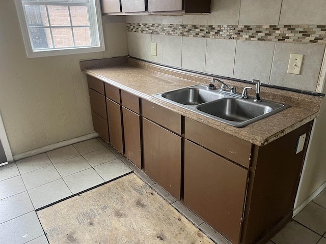 kitchen featuring light tile patterned floors, dark brown cabinets, backsplash, and a sink