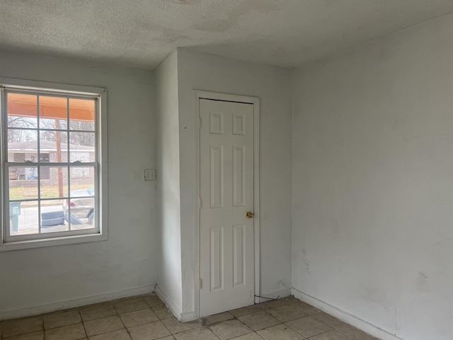 empty room featuring light tile patterned flooring, a textured ceiling, and baseboards