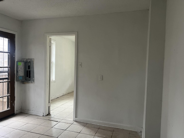 unfurnished room with a textured ceiling, light tile patterned floors, and baseboards