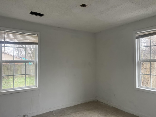 spare room with a wealth of natural light, a textured ceiling, and baseboards