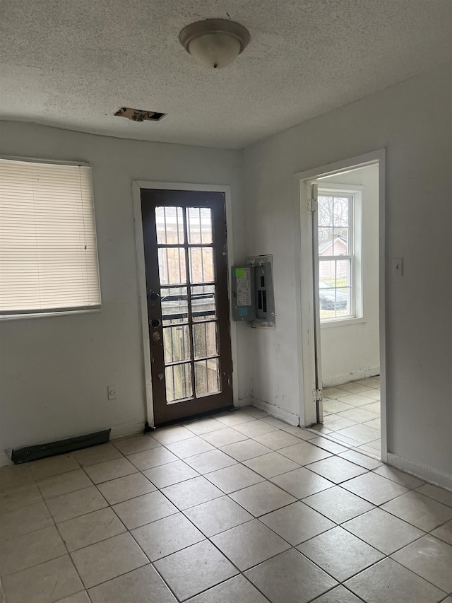 entryway with light tile patterned floors, visible vents, a textured ceiling, electric panel, and baseboards