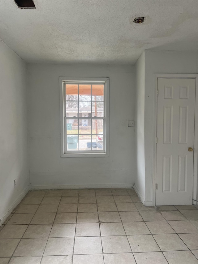 empty room featuring a textured ceiling, baseboards, and light tile patterned floors