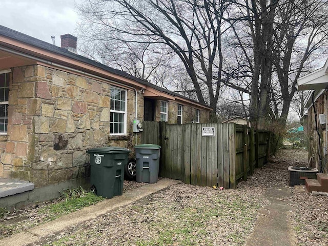 view of side of property featuring stone siding, a chimney, fence, and cooling unit