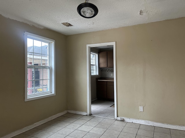 spare room with visible vents, a textured ceiling, baseboards, and light tile patterned floors