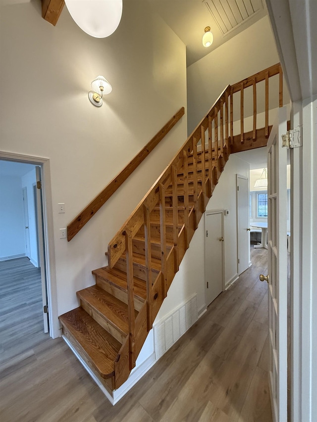 stairway with a high ceiling, wood finished floors, and visible vents