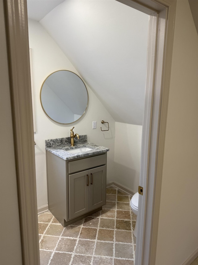 bathroom with lofted ceiling, baseboards, vanity, and toilet